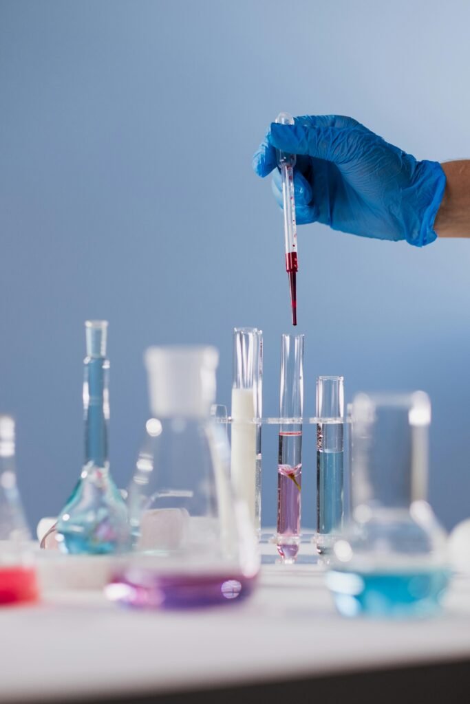 pexels-photo-10187144-10187144 A scientist's hand with a glove holding a dropper above test tubes with colorful liquids in a lab setting.